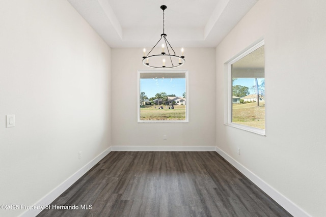 unfurnished dining area with a notable chandelier, dark hardwood / wood-style floors, and a raised ceiling