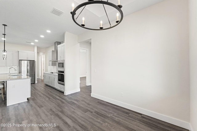 kitchen featuring sink, appliances with stainless steel finishes, white cabinetry, hanging light fixtures, and a center island with sink