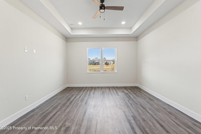 empty room featuring a raised ceiling, ceiling fan, and dark hardwood / wood-style flooring