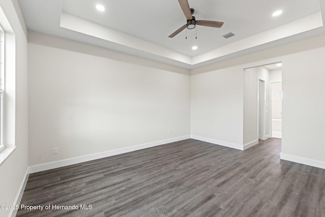 empty room with a tray ceiling, dark wood-type flooring, and ceiling fan