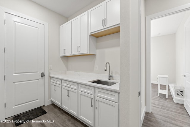 kitchen with sink, hardwood / wood-style floors, white cabinets, and light stone counters