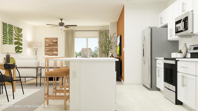 kitchen featuring ceiling fan, white cabinetry, stainless steel appliances, a center island, and a kitchen bar