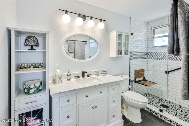 bathroom with tile patterned flooring, vanity, a tile shower, and toilet