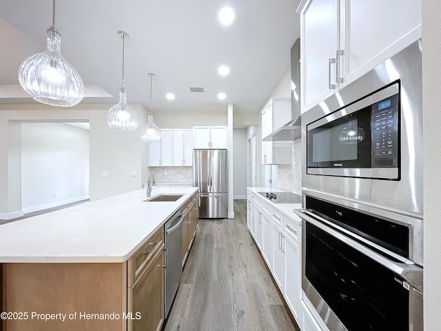 kitchen featuring an island with sink, appliances with stainless steel finishes, white cabinets, and wall chimney exhaust hood