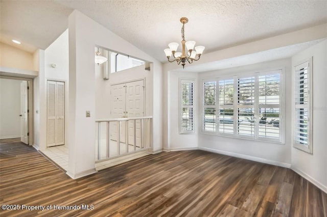 unfurnished dining area with lofted ceiling, a textured ceiling, dark hardwood / wood-style flooring, and a chandelier