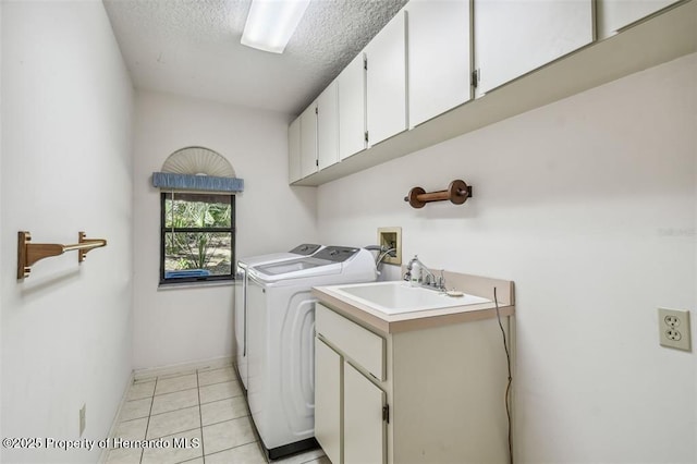 clothes washing area with sink, cabinets, a textured ceiling, washer and dryer, and light tile patterned floors