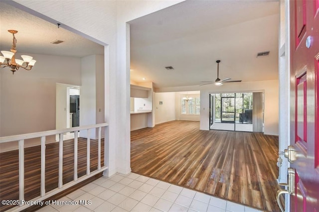 tiled empty room with lofted ceiling and ceiling fan with notable chandelier