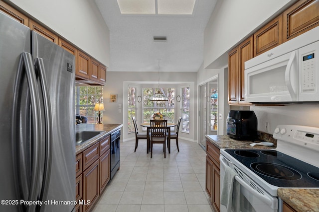 kitchen with light stone counters, hanging light fixtures, white appliances, and light tile patterned floors