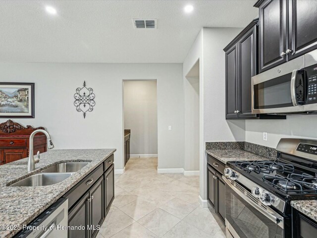 kitchen featuring light tile patterned flooring, stone countertops, sink, stainless steel appliances, and a textured ceiling