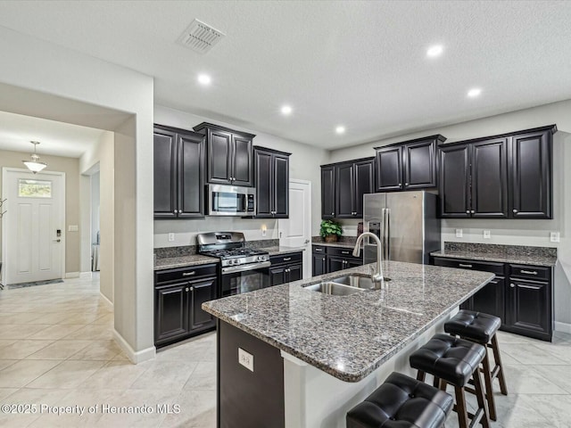 kitchen featuring appliances with stainless steel finishes, sink, dark stone countertops, a kitchen breakfast bar, and a center island with sink