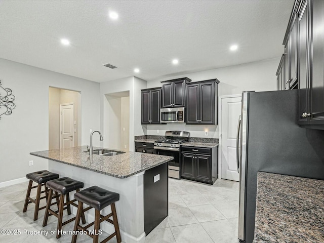 kitchen with sink, stainless steel appliances, an island with sink, and stone counters