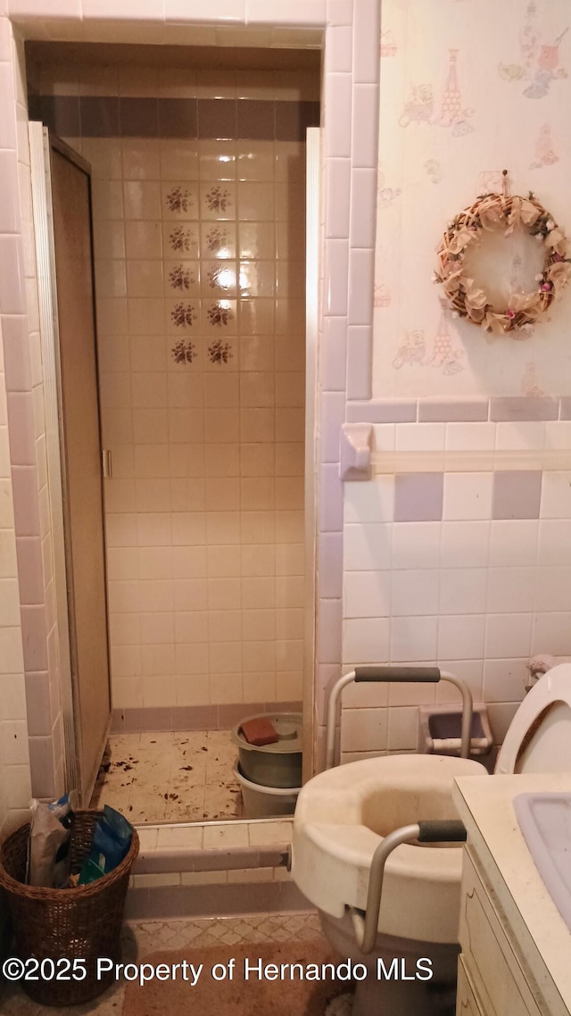 bathroom featuring tiled shower, vanity, and tile walls