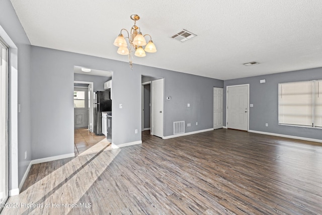 unfurnished living room featuring an inviting chandelier, visible vents, and wood finished floors