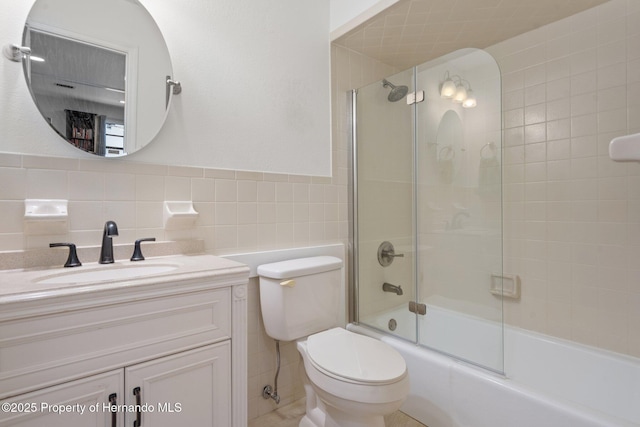 full bathroom featuring toilet, vanity, bath / shower combo with glass door, and tile walls