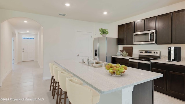 kitchen featuring stainless steel appliances, dark brown cabinets, a kitchen island with sink, and sink