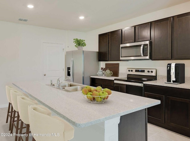 kitchen featuring sink, dark brown cabinets, stainless steel appliances, a center island with sink, and a kitchen bar