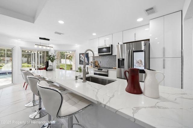 kitchen featuring a kitchen bar, decorative light fixtures, stainless steel appliances, light stone countertops, and white cabinets