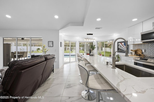 kitchen with sink, light stone counters, decorative light fixtures, appliances with stainless steel finishes, and white cabinets
