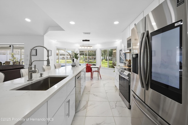 kitchen featuring white cabinetry, sink, decorative light fixtures, and appliances with stainless steel finishes