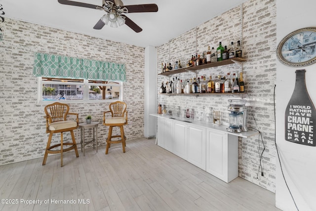 bar featuring ceiling fan, brick wall, and light hardwood / wood-style floors