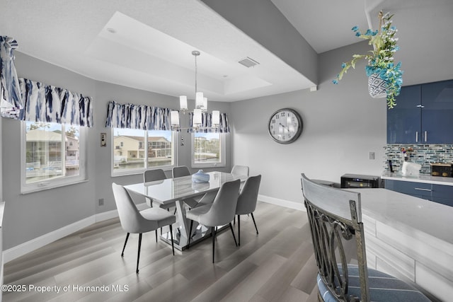 dining space featuring wood-type flooring, a chandelier, and a tray ceiling