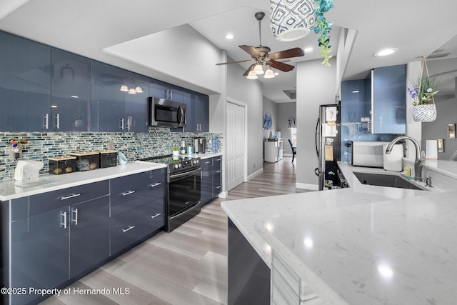 kitchen with blue cabinetry, appliances with stainless steel finishes, light stone countertops, and sink