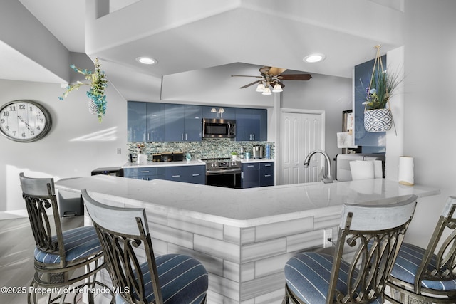 kitchen with tasteful backsplash, ceiling fan, kitchen peninsula, stainless steel appliances, and blue cabinetry