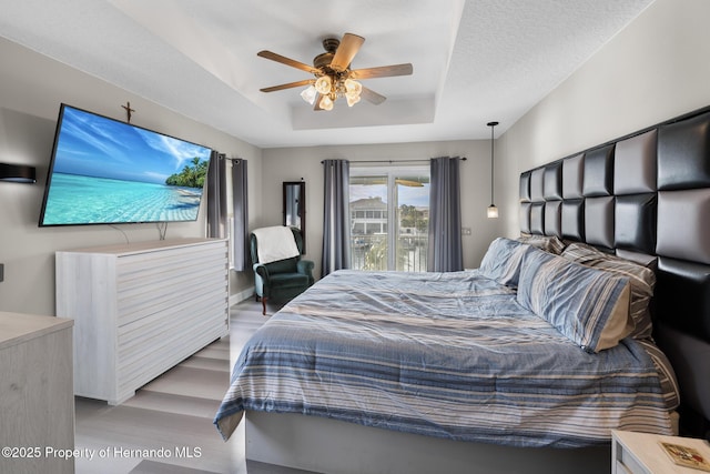 bedroom featuring ceiling fan, a tray ceiling, light hardwood / wood-style floors, and access to exterior