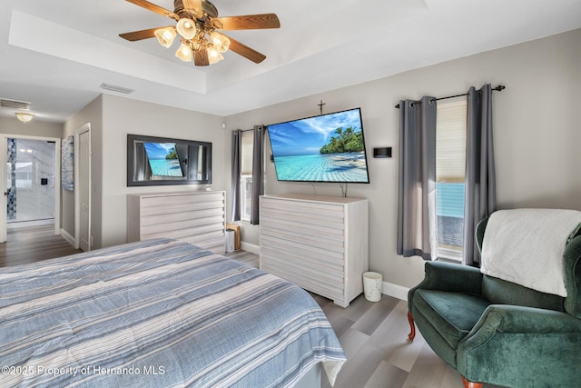 bedroom featuring ceiling fan, a tray ceiling, and light hardwood / wood-style flooring