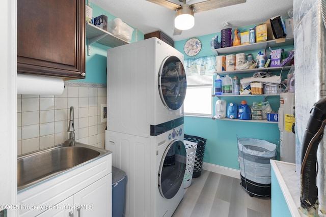 laundry area featuring stacked washer / dryer, water heater, sink, cabinets, and light hardwood / wood-style floors