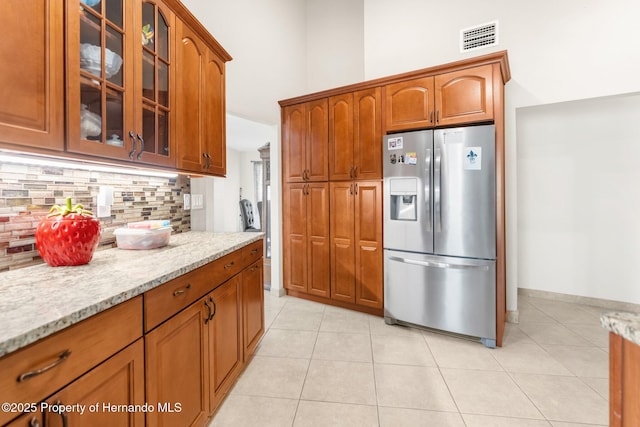 kitchen featuring light tile patterned floors, a high ceiling, light stone counters, stainless steel fridge with ice dispenser, and decorative backsplash