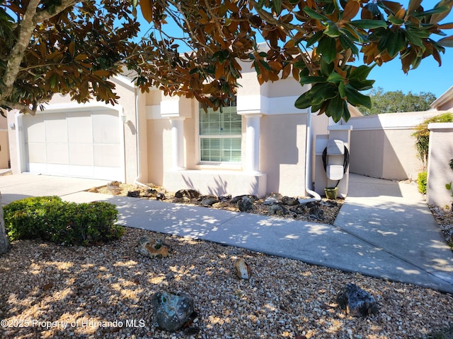 view of front of property with stucco siding, concrete driveway, a garage, and fence