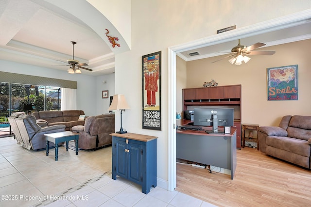 living room featuring ceiling fan, ornamental molding, a tray ceiling, and light tile patterned floors