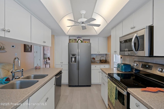 kitchen with sink, appliances with stainless steel finishes, white cabinetry, a tray ceiling, and decorative backsplash