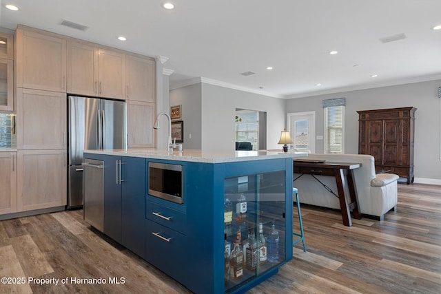 kitchen featuring stainless steel appliances, visible vents, light brown cabinets, an island with sink, and wood finished floors