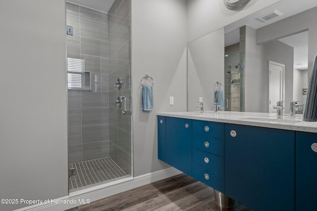 bathroom with double vanity, visible vents, a sink, a shower stall, and wood finished floors