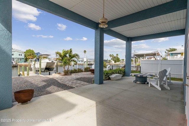 view of patio featuring a water view, fence, boat lift, and a boat dock