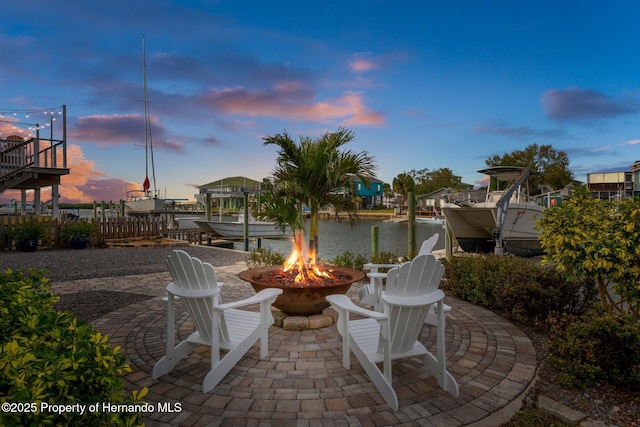 patio terrace at dusk featuring an outdoor fire pit, a boat dock, a water view, and boat lift