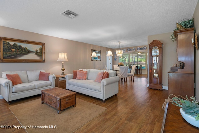 living area featuring a textured ceiling, dark wood-type flooring, visible vents, and a notable chandelier