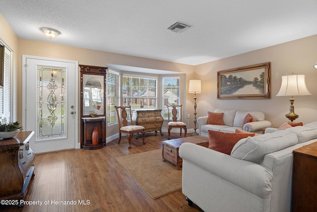 living room featuring a textured ceiling, wood finished floors, visible vents, and baseboards