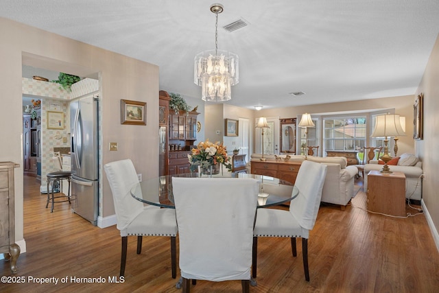 dining space with baseboards, visible vents, an inviting chandelier, and wood finished floors