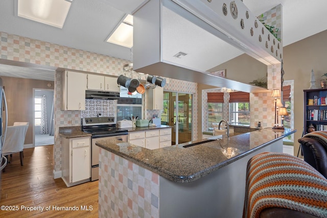 kitchen with white cabinets, dark stone countertops, a peninsula, stainless steel electric stove, and under cabinet range hood