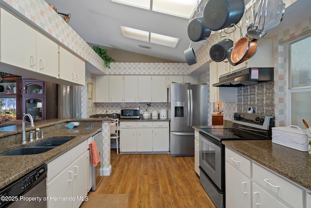 kitchen featuring under cabinet range hood, a sink, white cabinetry, appliances with stainless steel finishes, and dark stone counters