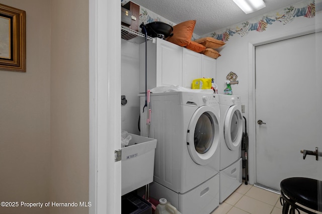 clothes washing area featuring washer and clothes dryer, light tile patterned floors, cabinet space, a sink, and a textured ceiling