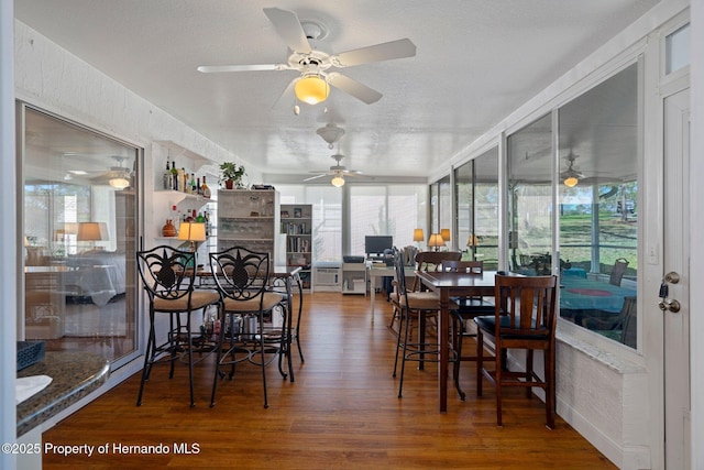 dining space featuring a sunroom, plenty of natural light, a textured ceiling, and wood finished floors