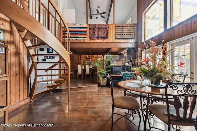 dining room with ceiling fan, a high ceiling, and wood walls