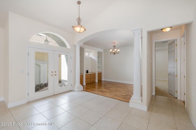 tiled entryway with french doors, high vaulted ceiling, an inviting chandelier, and decorative columns