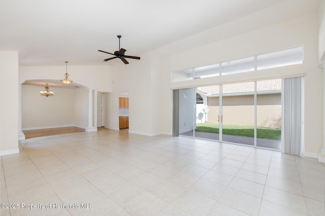 tiled empty room with decorative columns, ceiling fan with notable chandelier, and high vaulted ceiling