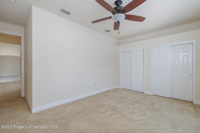 unfurnished bedroom with two closets, light carpet, and ceiling fan