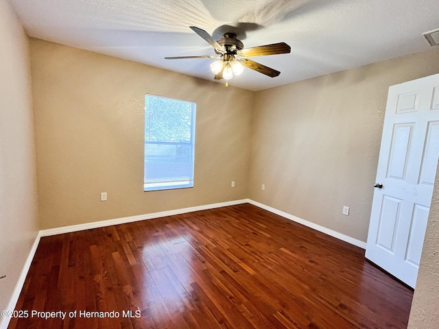 unfurnished room featuring ceiling fan, visible vents, baseboards, and dark wood finished floors